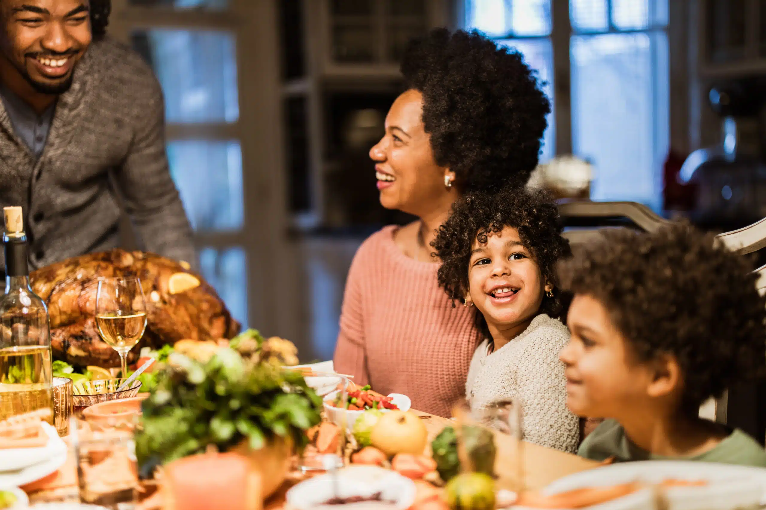 A family of four enjoys a Thanksgiving dinner together at a festive table. The mother and father are smiling while the children sit in front of an array of food, including a large roasted turkey. They were thrilled to save money on their holiday feast without compromising on quality or taste.