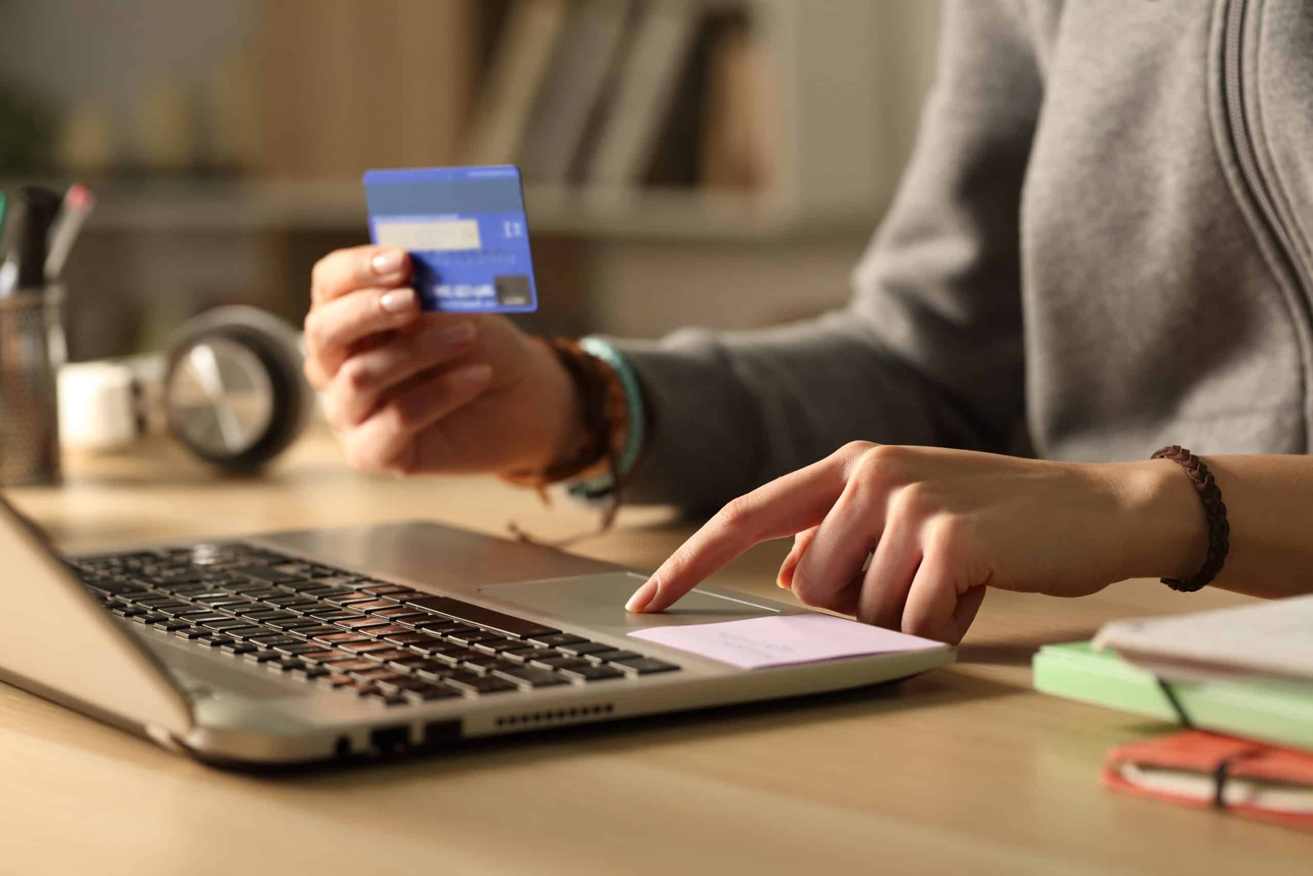 A person uses a laptop while holding a credit card, appearing to make an online purchase.